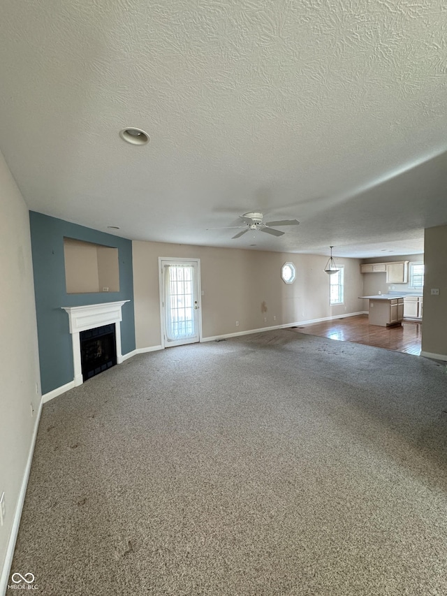 unfurnished living room with carpet, plenty of natural light, a textured ceiling, and ceiling fan