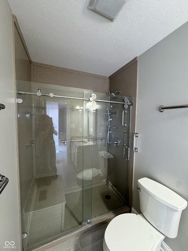 bathroom with walk in shower, toilet, and a textured ceiling