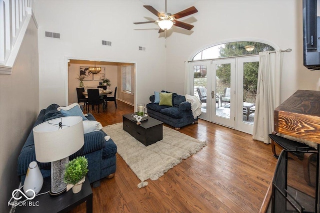 living room featuring hardwood / wood-style floors, ceiling fan with notable chandelier, french doors, and a high ceiling