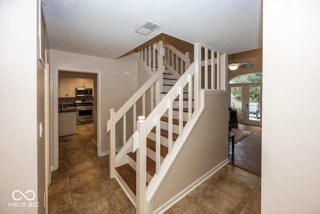 stairs featuring french doors, ceiling fan, tile patterned flooring, and a textured ceiling