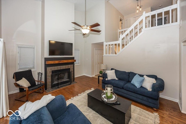 living room featuring a fireplace, wood-type flooring, ceiling fan, and a high ceiling