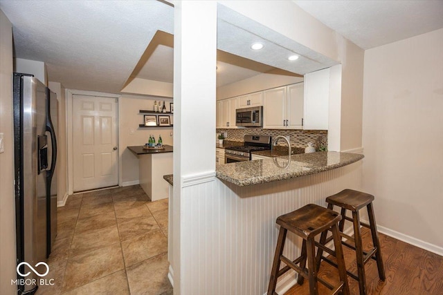 kitchen featuring appliances with stainless steel finishes, white cabinets, a kitchen bar, dark stone counters, and kitchen peninsula