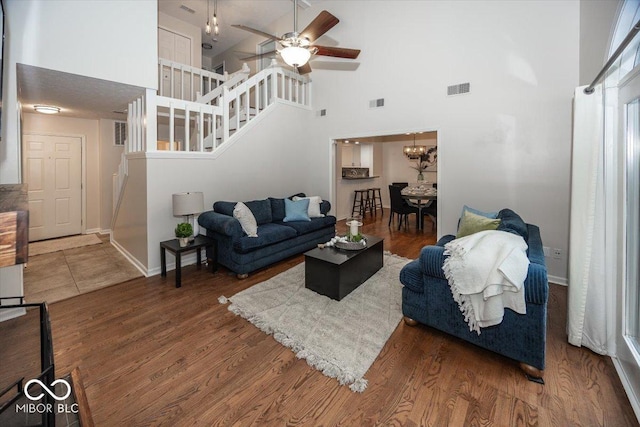 living room with a towering ceiling, dark hardwood / wood-style floors, and ceiling fan with notable chandelier