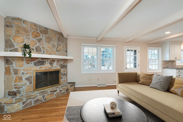 living room with light hardwood / wood-style floors, beamed ceiling, and a fireplace