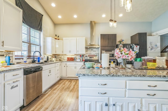 kitchen with pendant lighting, wall chimney range hood, sink, stainless steel appliances, and white cabinets