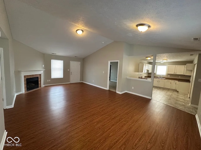 unfurnished living room with vaulted ceiling, dark hardwood / wood-style floors, a wealth of natural light, and a textured ceiling