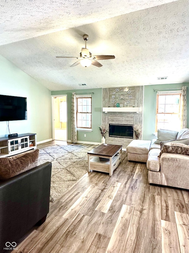 living room featuring vaulted ceiling, a textured ceiling, a large fireplace, ceiling fan, and hardwood / wood-style floors