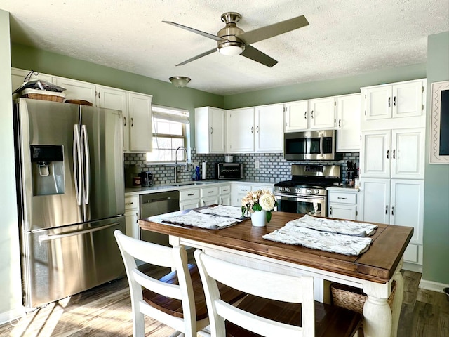 kitchen with sink, light hardwood / wood-style flooring, appliances with stainless steel finishes, white cabinets, and decorative backsplash