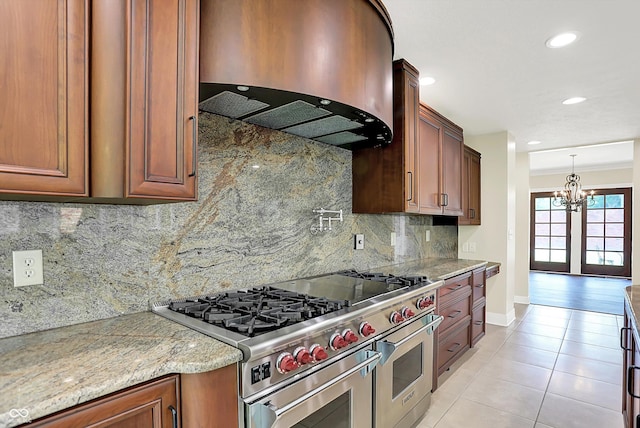 8602 Frontgate Ln, Indianapolis, IN 46256 - kitchen with range with two ovens, wall chimney range hood, a chandelier, light tile patterned floors, and baseboards