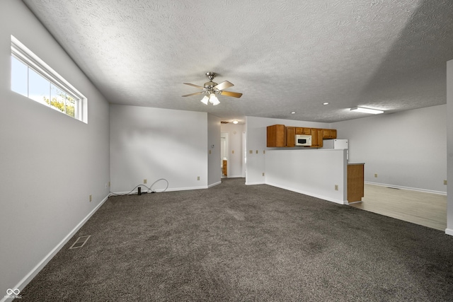 unfurnished living room with ceiling fan, a textured ceiling, and dark carpet