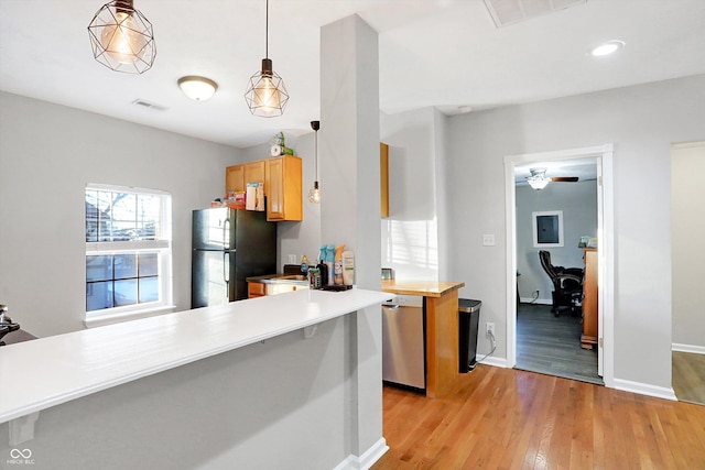 kitchen featuring decorative light fixtures, light wood-type flooring, black refrigerator, dishwasher, and kitchen peninsula