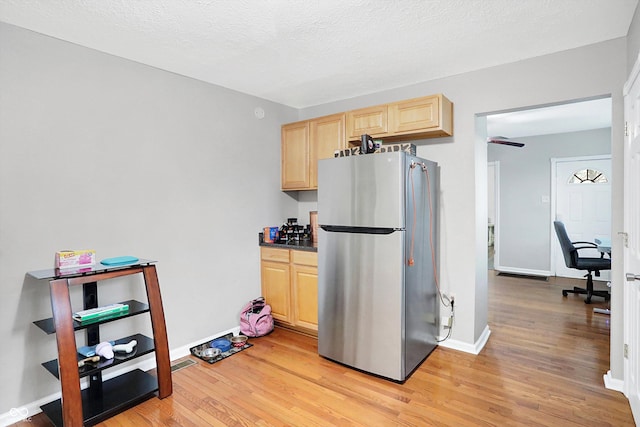 kitchen with light wood-type flooring, a textured ceiling, stainless steel fridge, and light brown cabinetry