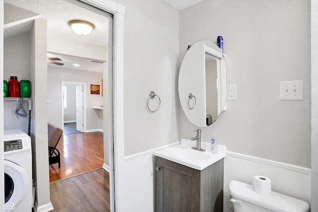 bathroom featuring toilet, washer / dryer, vanity, hardwood / wood-style flooring, and ceiling fan