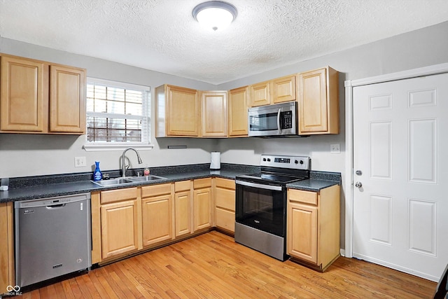 kitchen with appliances with stainless steel finishes, light brown cabinetry, sink, light wood-type flooring, and a textured ceiling