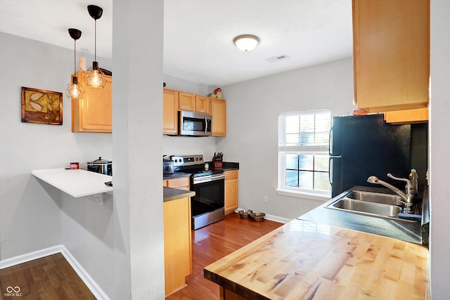 kitchen with sink, hanging light fixtures, light brown cabinets, stainless steel appliances, and hardwood / wood-style floors