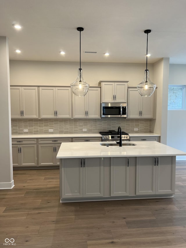 kitchen with decorative backsplash, dark wood finished floors, light countertops, a sink, and stainless steel microwave