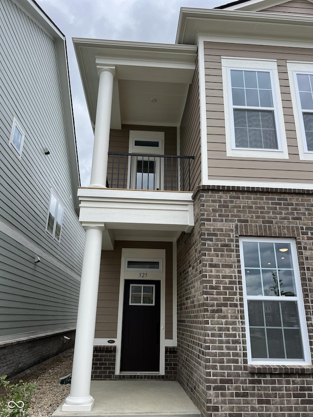 entrance to property with covered porch, brick siding, and a balcony