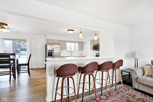 kitchen featuring gray cabinets, appliances with stainless steel finishes, wood-type flooring, hanging light fixtures, and kitchen peninsula