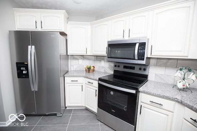 kitchen featuring white cabinetry, dark tile patterned flooring, light stone counters, and stainless steel appliances