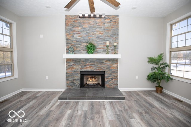 unfurnished living room featuring ceiling fan, a healthy amount of sunlight, wood-type flooring, and a stone fireplace