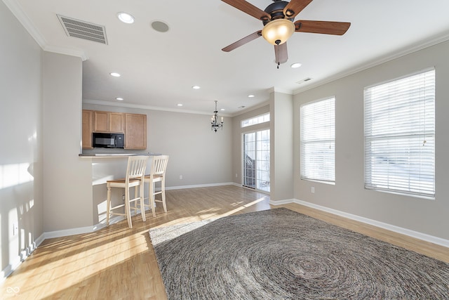 kitchen featuring crown molding, ceiling fan with notable chandelier, light hardwood / wood-style floors, and a breakfast bar area