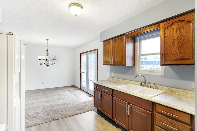 kitchen with sink, decorative light fixtures, a textured ceiling, light wood-type flooring, and a notable chandelier