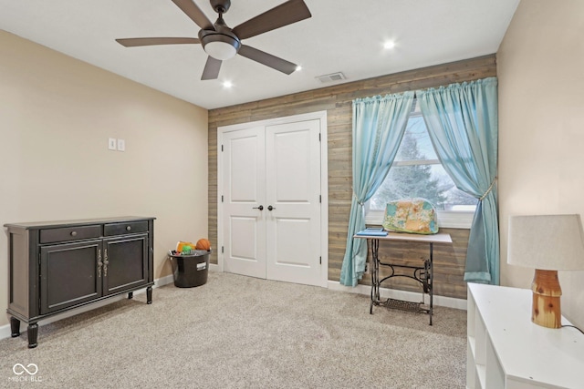 interior space with ceiling fan, wooden walls, and light carpet