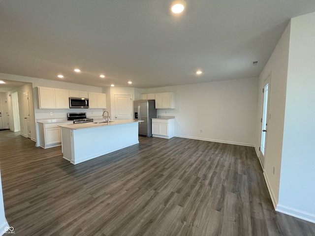 kitchen featuring sink, dark wood-type flooring, appliances with stainless steel finishes, white cabinets, and a center island with sink