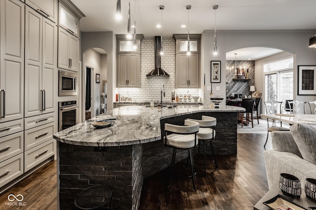 kitchen featuring pendant lighting, sink, appliances with stainless steel finishes, an island with sink, and wall chimney exhaust hood