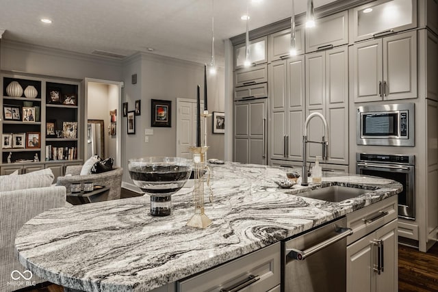 kitchen featuring sink, hanging light fixtures, a center island with sink, stainless steel appliances, and light stone countertops