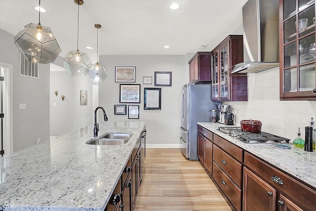 kitchen featuring an island with sink, sink, decorative backsplash, light stone counters, and wall chimney range hood