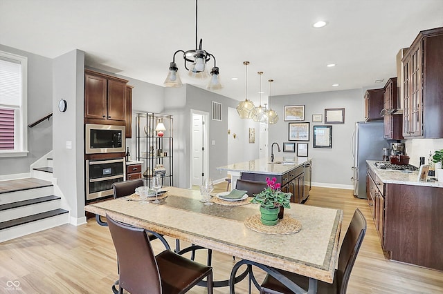 kitchen featuring appliances with stainless steel finishes, decorative light fixtures, light hardwood / wood-style floors, light stone countertops, and a center island with sink