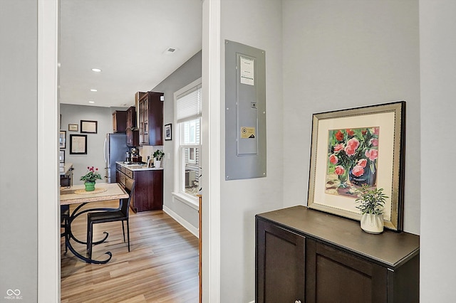 kitchen featuring dark brown cabinets, electric panel, stainless steel refrigerator, and light wood-type flooring