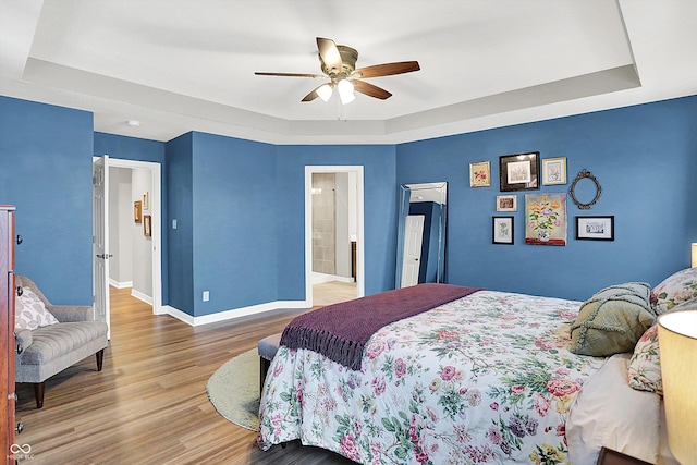 bedroom with hardwood / wood-style floors, a tray ceiling, and ceiling fan