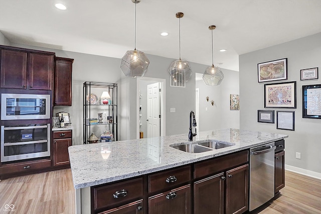 kitchen with sink, light stone counters, hanging light fixtures, an island with sink, and stainless steel appliances