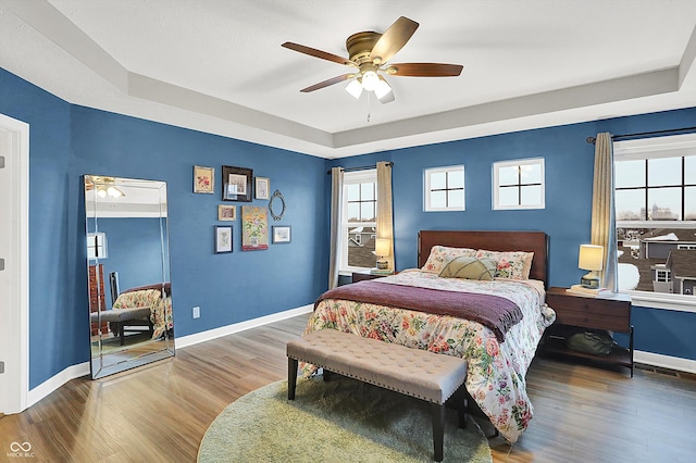 bedroom with ceiling fan, wood-type flooring, and a tray ceiling