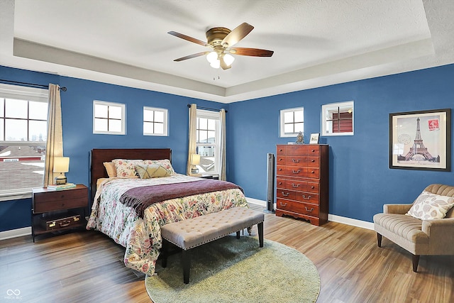 bedroom featuring hardwood / wood-style flooring, ceiling fan, a tray ceiling, and a textured ceiling