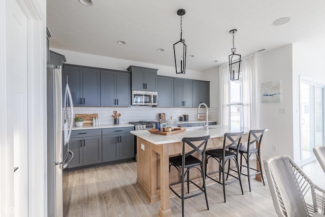 kitchen with sink, tasteful backsplash, decorative light fixtures, a center island with sink, and stainless steel appliances