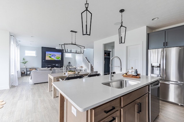 kitchen with pendant lighting, stainless steel appliances, sink, and a kitchen island with sink