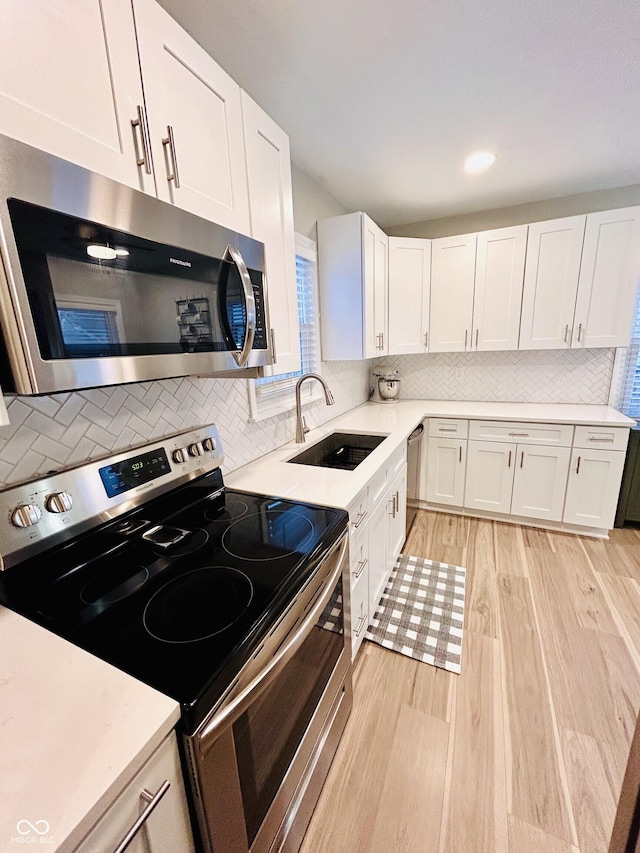 kitchen featuring sink, stainless steel appliances, tasteful backsplash, light hardwood / wood-style floors, and white cabinets