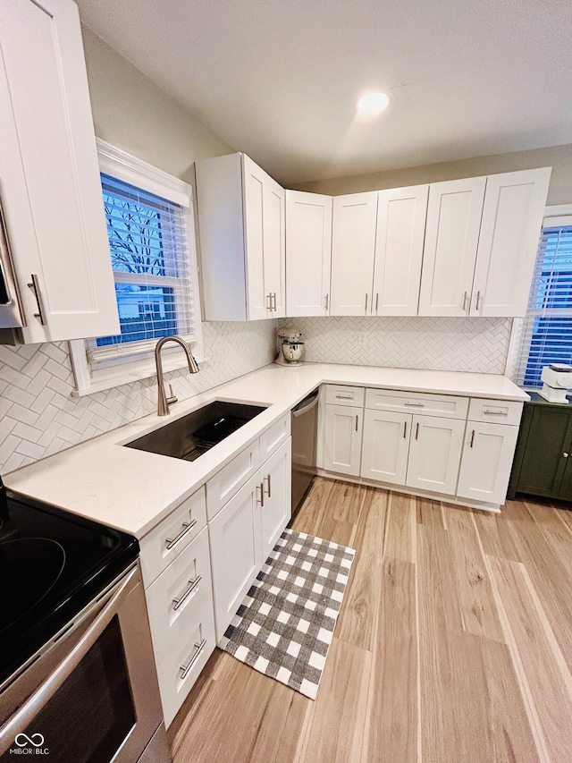 kitchen featuring white cabinetry, sink, backsplash, stainless steel appliances, and light hardwood / wood-style flooring