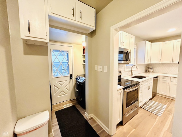 kitchen featuring appliances with stainless steel finishes, white cabinetry, sink, decorative backsplash, and light wood-type flooring