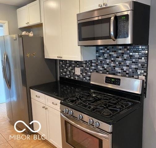 kitchen with light tile patterned flooring, appliances with stainless steel finishes, white cabinets, backsplash, and dark stone counters