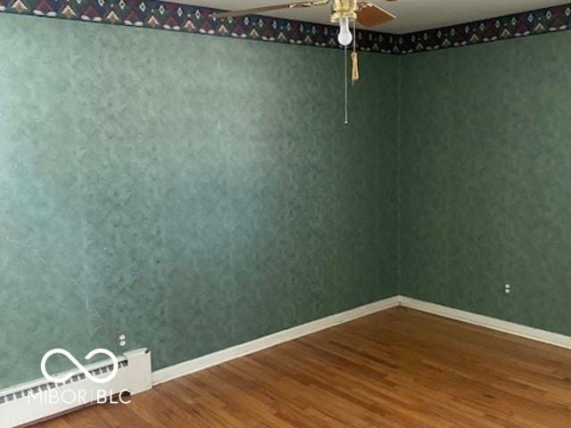 spare room featuring hardwood / wood-style flooring, ceiling fan, and a baseboard heating unit