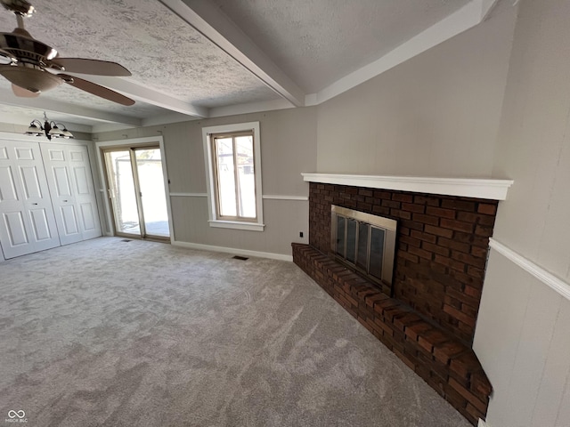 unfurnished living room featuring beam ceiling, carpet, ceiling fan, a brick fireplace, and a textured ceiling