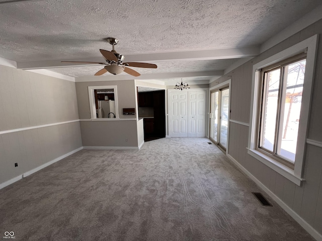 unfurnished living room with a textured ceiling, a wealth of natural light, beamed ceiling, and carpet flooring