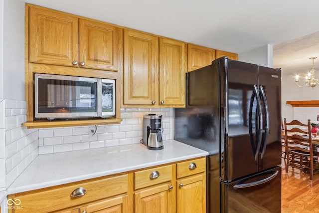 kitchen featuring hardwood / wood-style flooring, black fridge, an inviting chandelier, and decorative backsplash