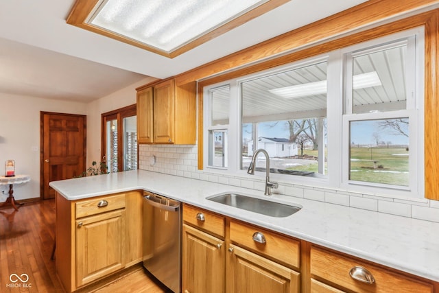 kitchen featuring sink, dishwasher, kitchen peninsula, light hardwood / wood-style floors, and decorative backsplash