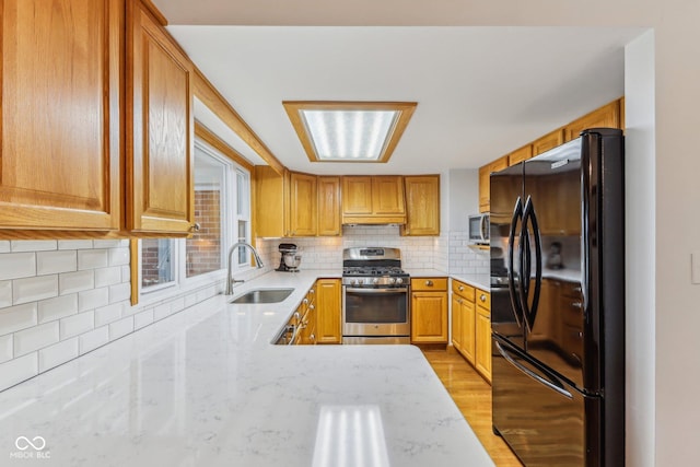 kitchen with sink, appliances with stainless steel finishes, light stone countertops, decorative backsplash, and light wood-type flooring