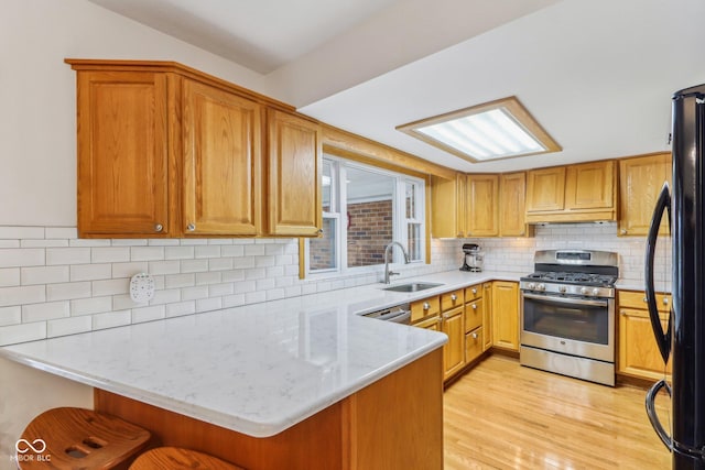 kitchen with sink, a kitchen bar, kitchen peninsula, stainless steel range with gas stovetop, and light wood-type flooring